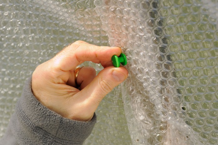 Pinning overlapping layers of bubble-wrap to the wooden frame of a greenhouse Pinning overlapping layers of bubble-wrap to the wooden frame of a greenhouse